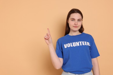 Photo of Portrait of woman in t-shirt with word Volunteer pointing at something on beige background. Space for text