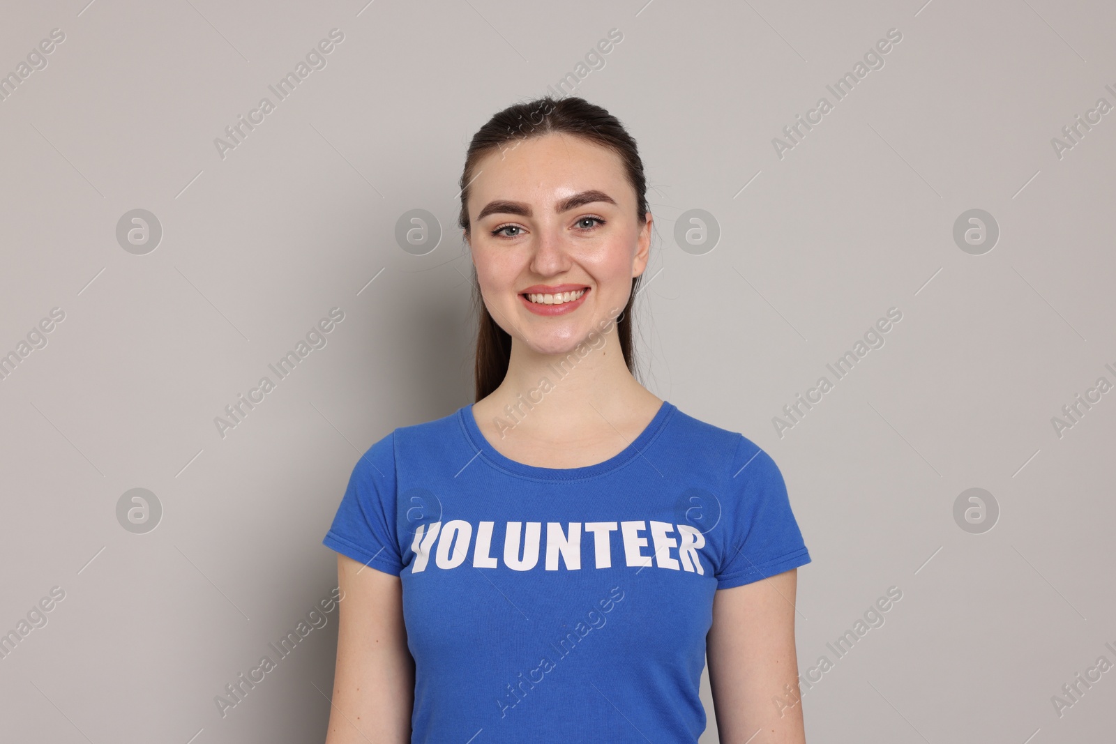 Photo of Portrait of smiling woman in t-shirt with word Volunteer on grey background