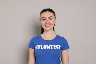 Photo of Portrait of smiling woman in t-shirt with word Volunteer on grey background