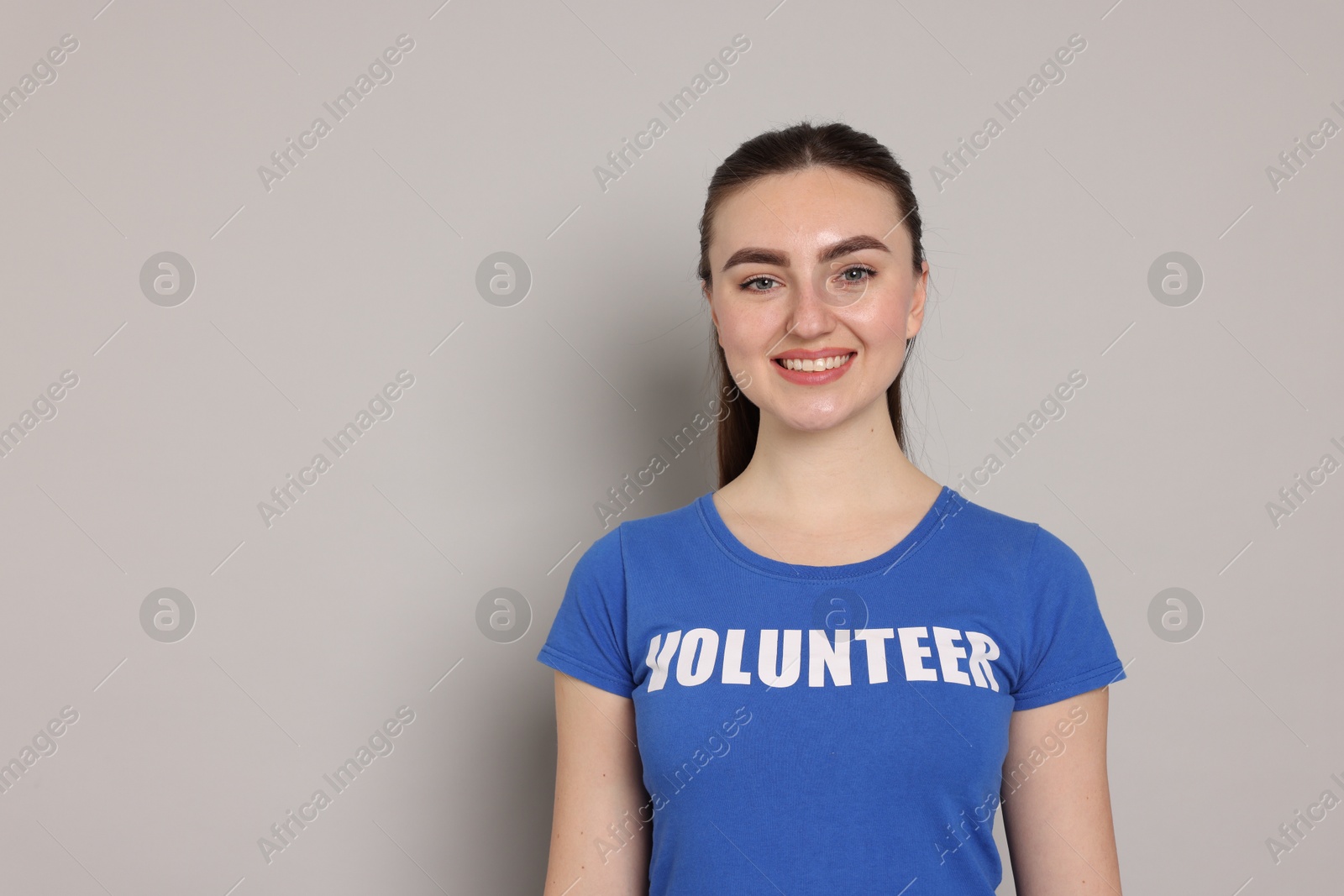 Photo of Portrait of smiling woman in t-shirt with word Volunteer on grey background. Space for text