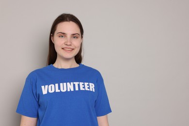 Photo of Portrait of smiling woman in t-shirt with word Volunteer on grey background. Space for text