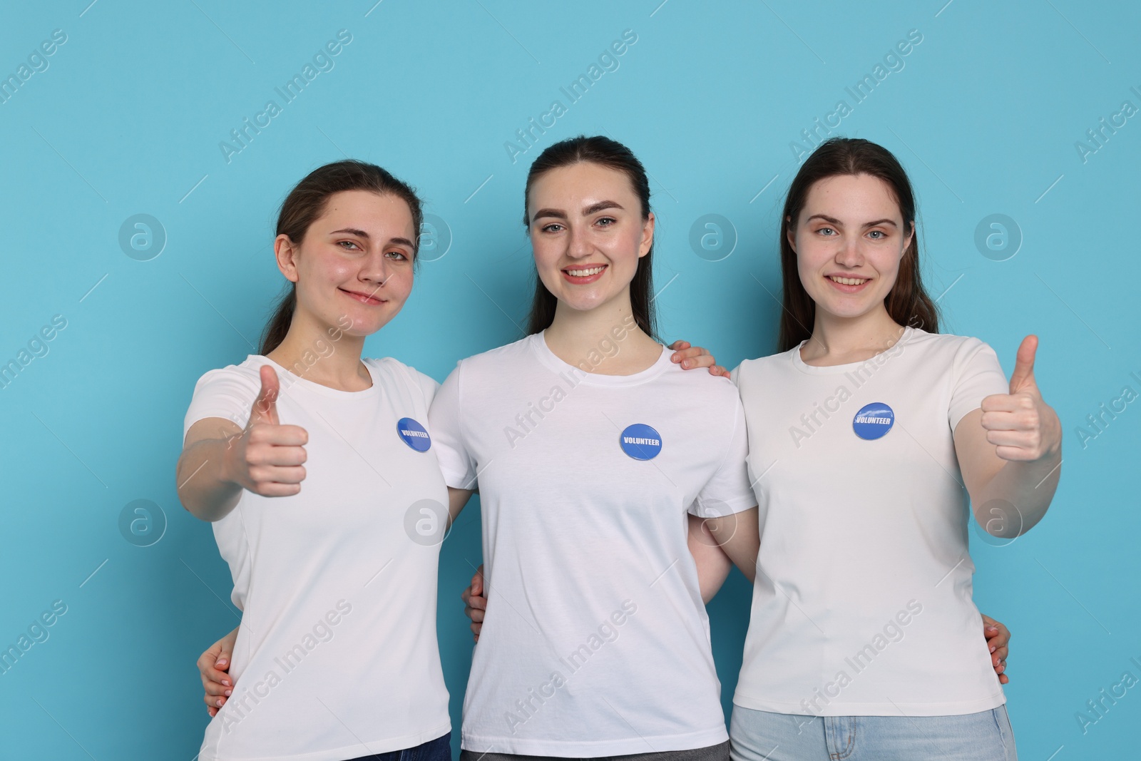 Photo of Team of smiling volunteers showing thumbs up on light blue background