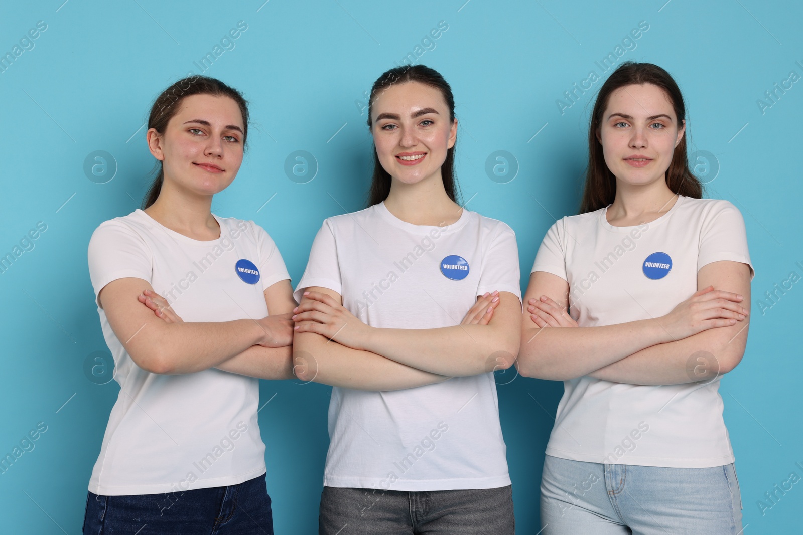 Photo of Team of smiling volunteers with crossed arms on light blue background