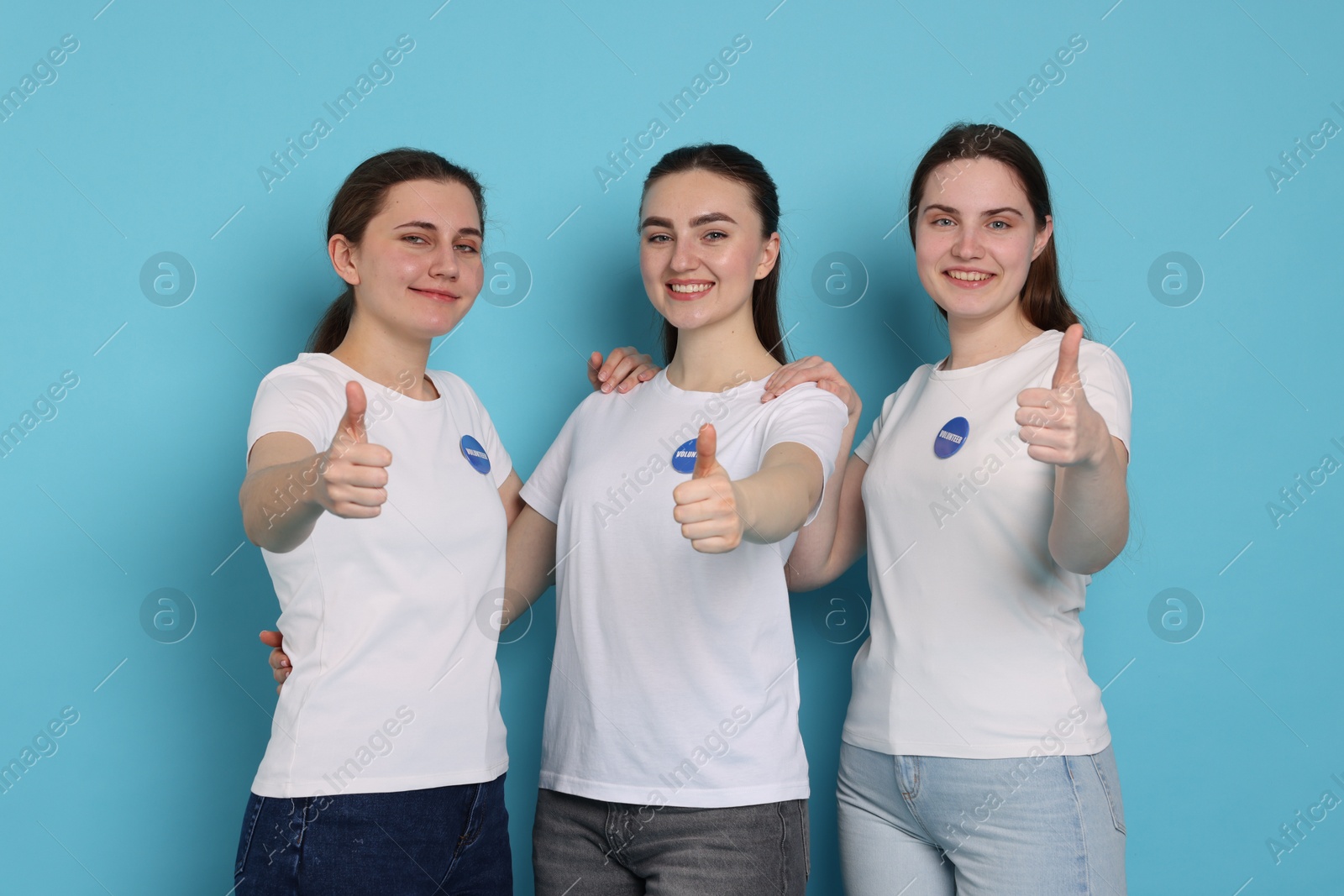 Photo of Team of smiling volunteers showing thumbs up on light blue background