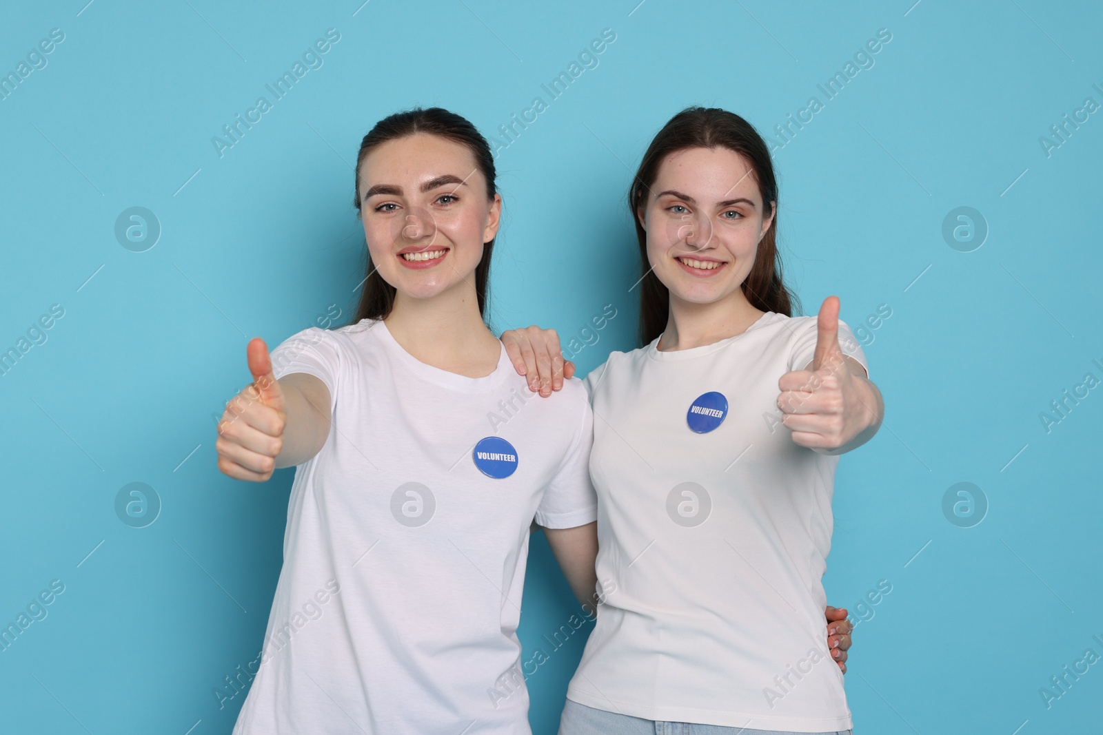 Photo of Smiling volunteers showing thumbs up on light blue background