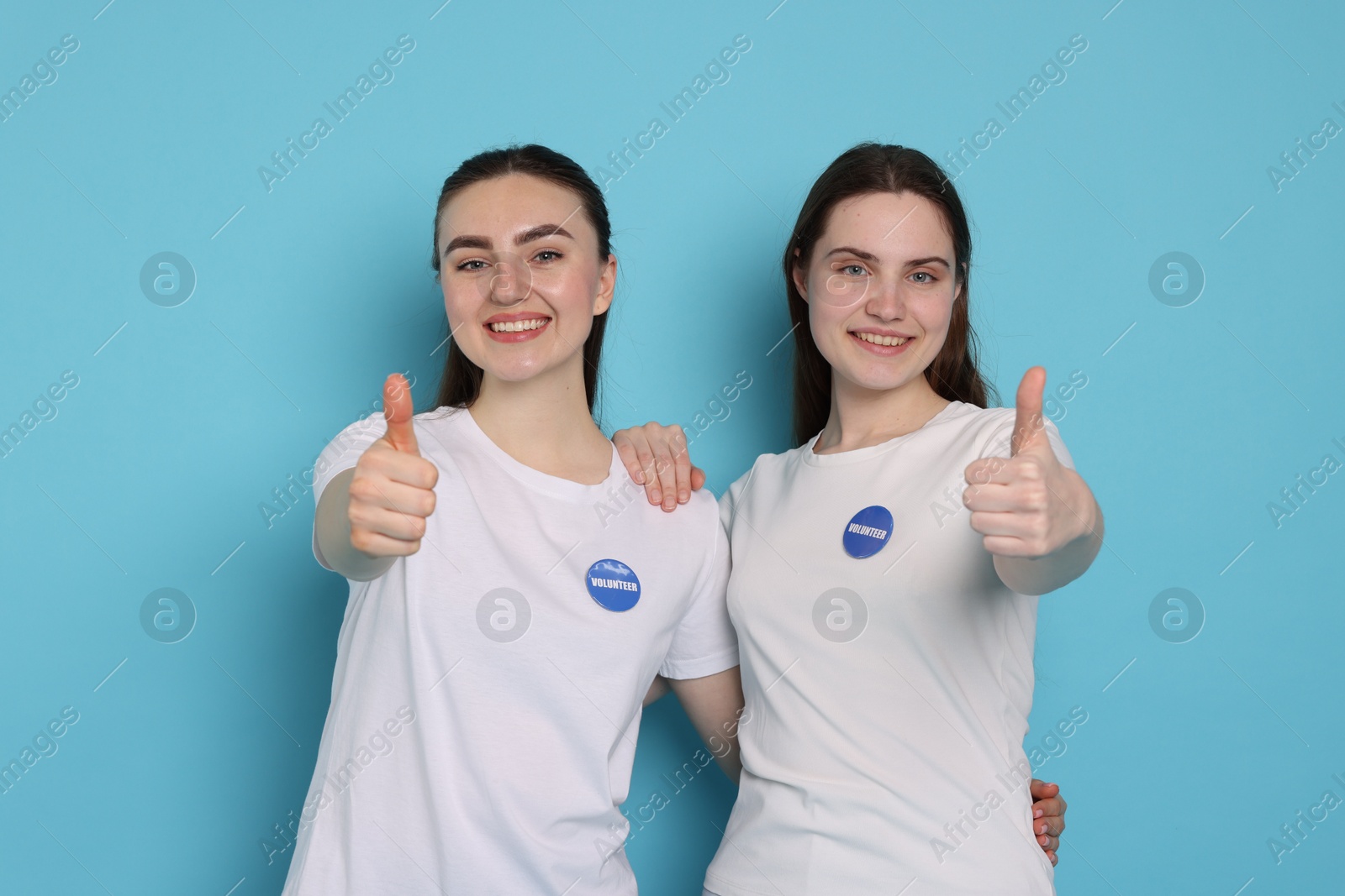 Photo of Smiling volunteers showing thumbs up on light blue background