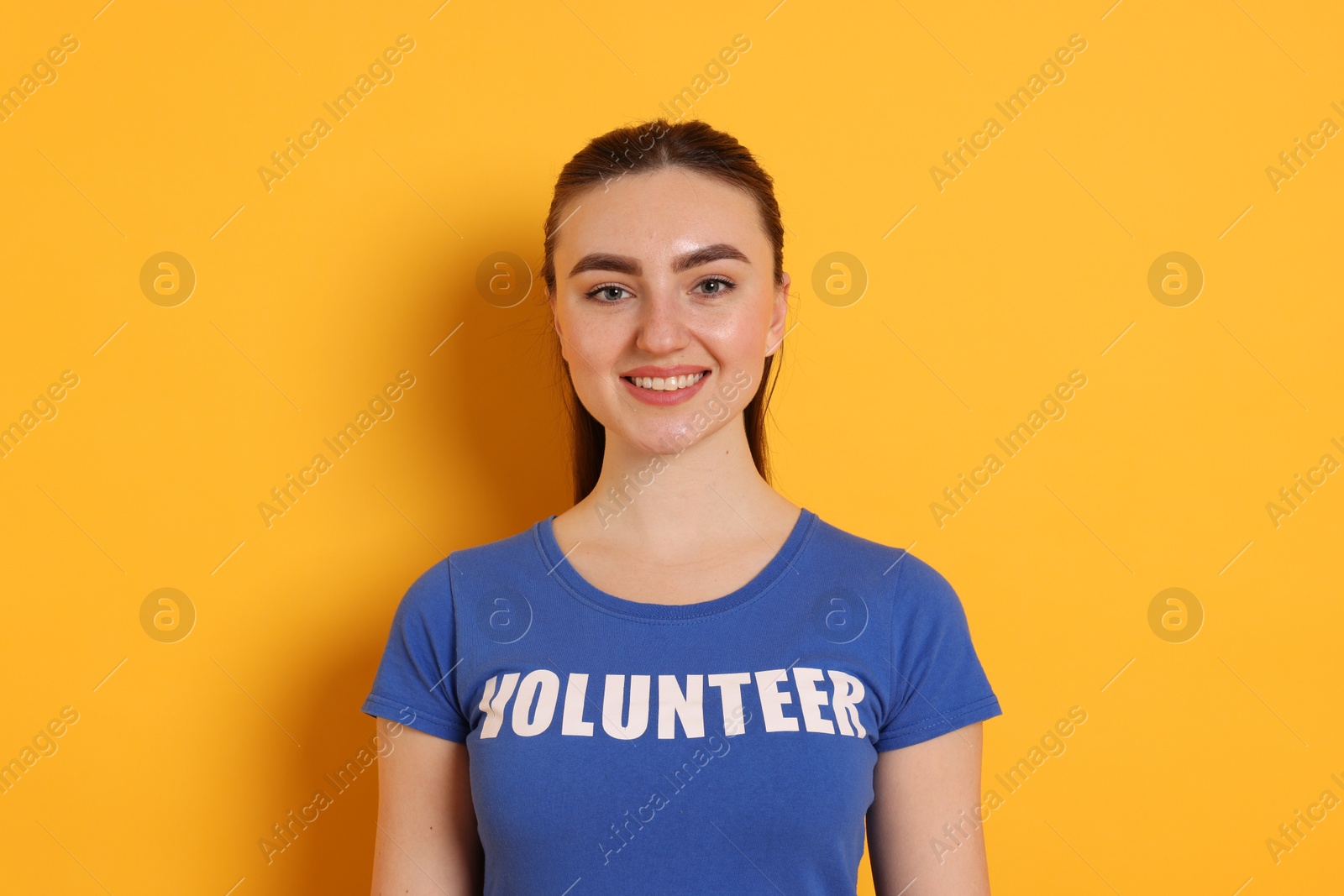 Photo of Portrait of smiling woman in t-shirt with word Volunteer on orange background