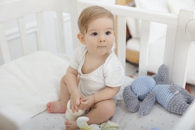 Photo of Cute little baby with feeding bottle of milk in crib at home