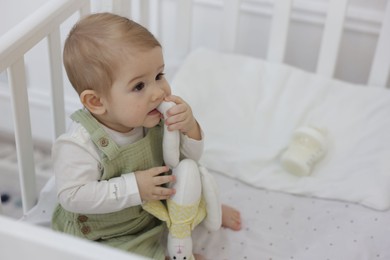 Photo of Cute little baby with toy bunny and feeding bottle of milk in crib at home, space for text