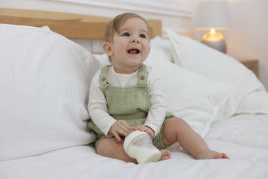 Photo of Cute little baby with feeding bottle of milk on bed at home