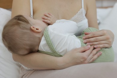 Mother breastfeeding her little baby on bed at home, closeup