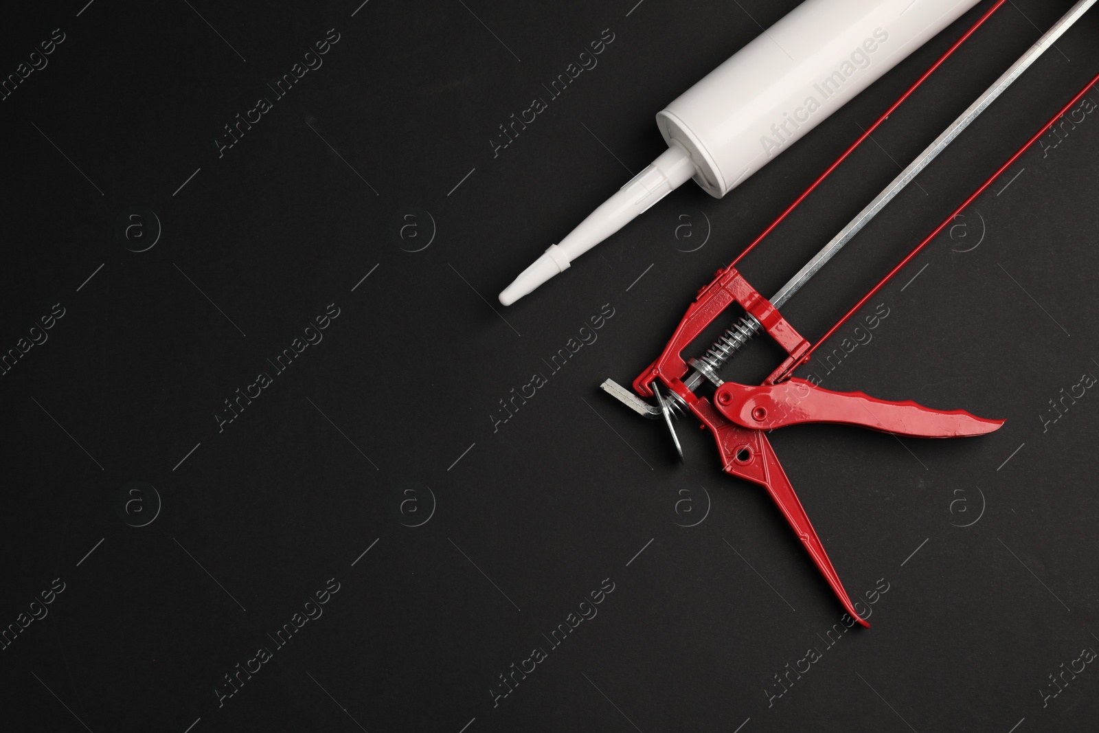 Photo of Glue gun and tube on black background, flat lay. Space for text