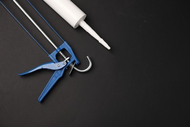 Photo of Glue gun and tube on black background, flat lay. Space for text