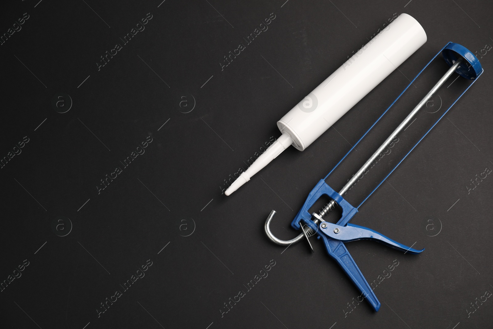 Photo of Glue gun and tube on black background, flat lay. Space for text