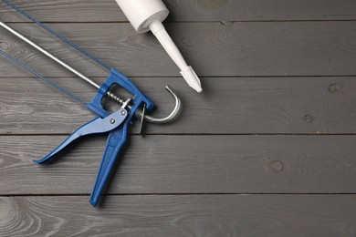 Glue gun and tube on gray wooden background, flat lay. Space for text