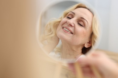 Photo of Smiling middle aged woman with round mirror on blurred background