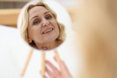 Photo of Smiling middle aged woman with round mirror on blurred background