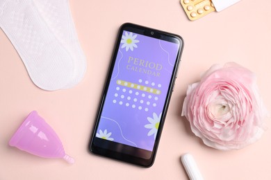 Photo of Smartphone with period calendar application, menstrual products and flower on beige background, flat lay