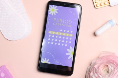 Photo of Smartphone with period calendar application, menstrual products and flower on beige background, flat lay