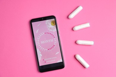 Photo of Smartphone with period calendar application and tampons on pink background, flat lay