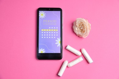 Photo of Smartphone with period calendar application, tampons and flower on pink background, flat lay