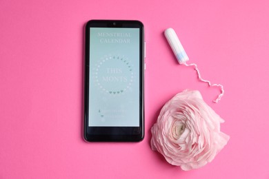 Photo of Smartphone with period calendar application, tampon and flower on pink background, flat lay