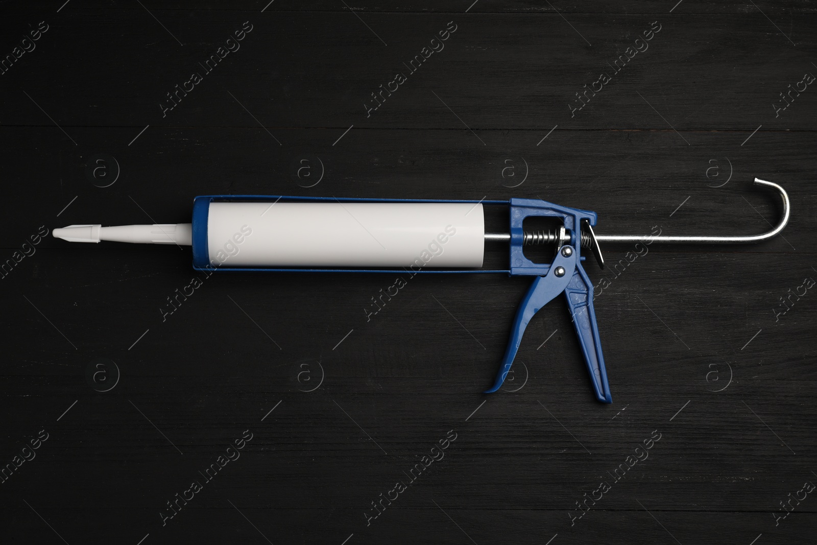 Photo of One glue gun on black wooden background, top view. Construction tool