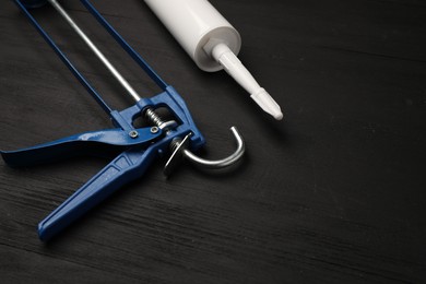 Photo of One glue gun and tube on black wooden background, closeup. Construction tool