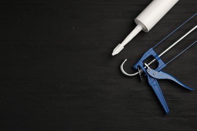 One glue gun and tube on black wooden background, top view with space for text. Construction tool