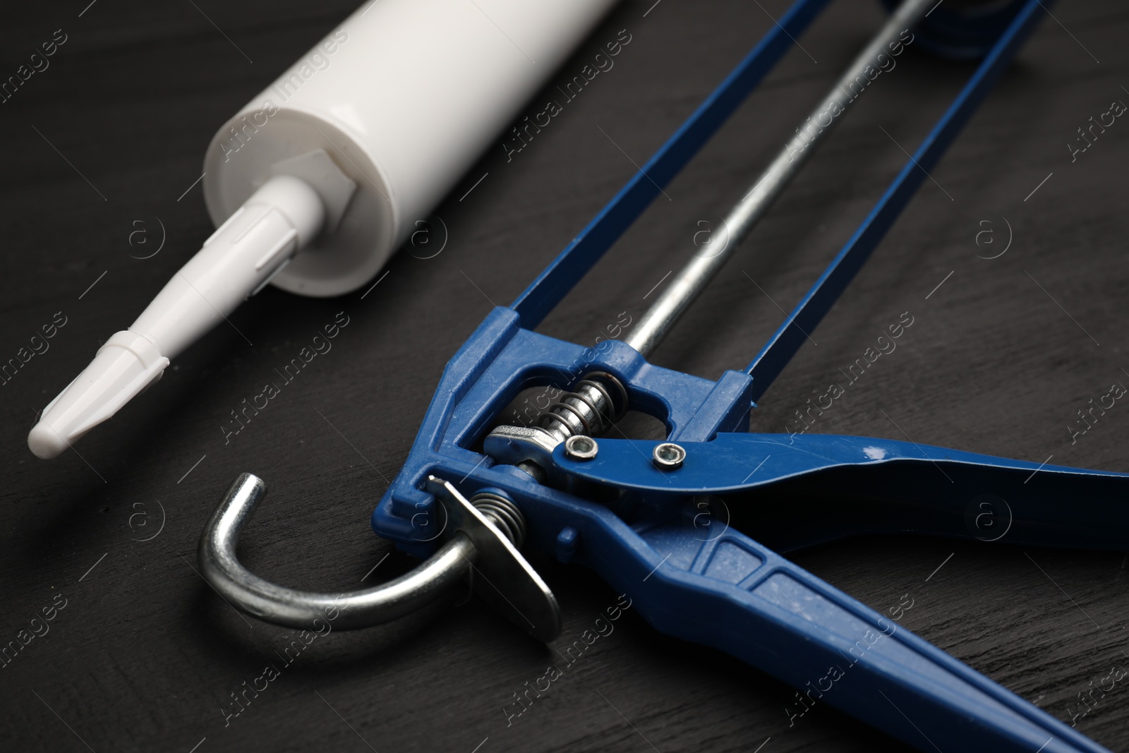 Photo of One glue gun and tube on black wooden background, closeup. Construction tool