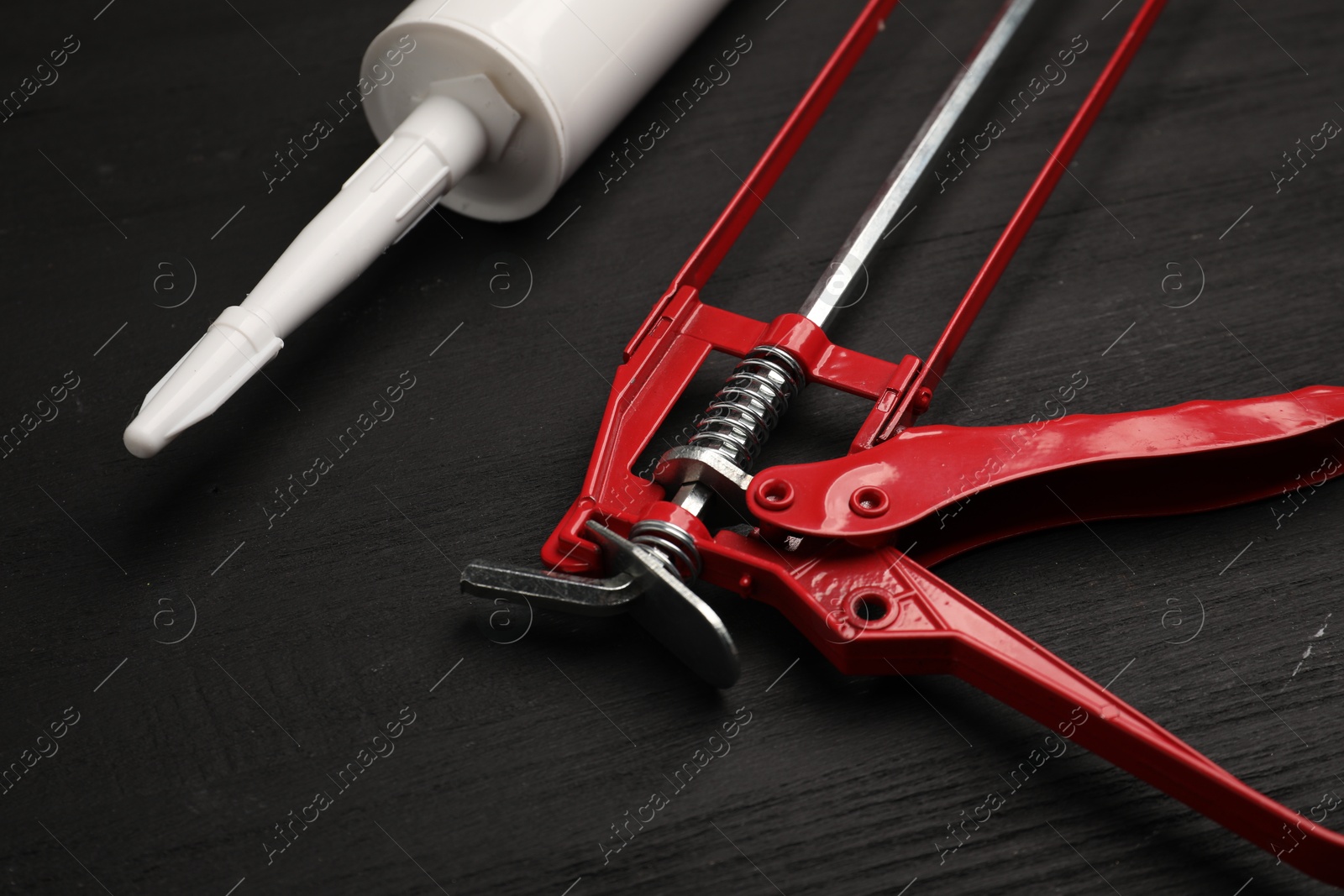 Photo of One glue gun and tube on black wooden background, closeup. Construction tool