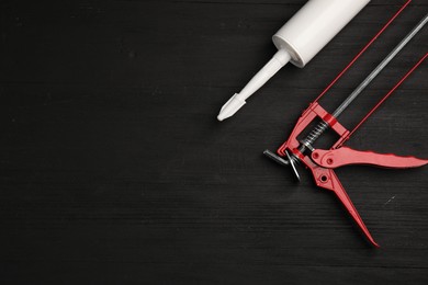 One glue gun and tube on black wooden background, top view with space for text. Construction tool