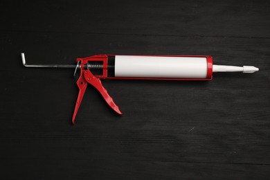 Photo of One glue gun on black wooden background, top view. Construction tool