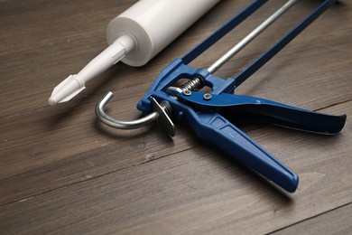 Photo of One glue gun and tube on wooden background, closeup. Construction tool