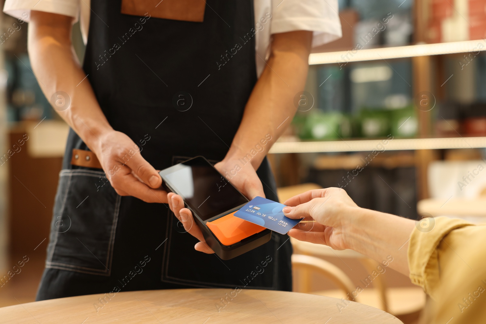 Photo of Woman paying with credit card via terminal at wooden table in cafe, closeup