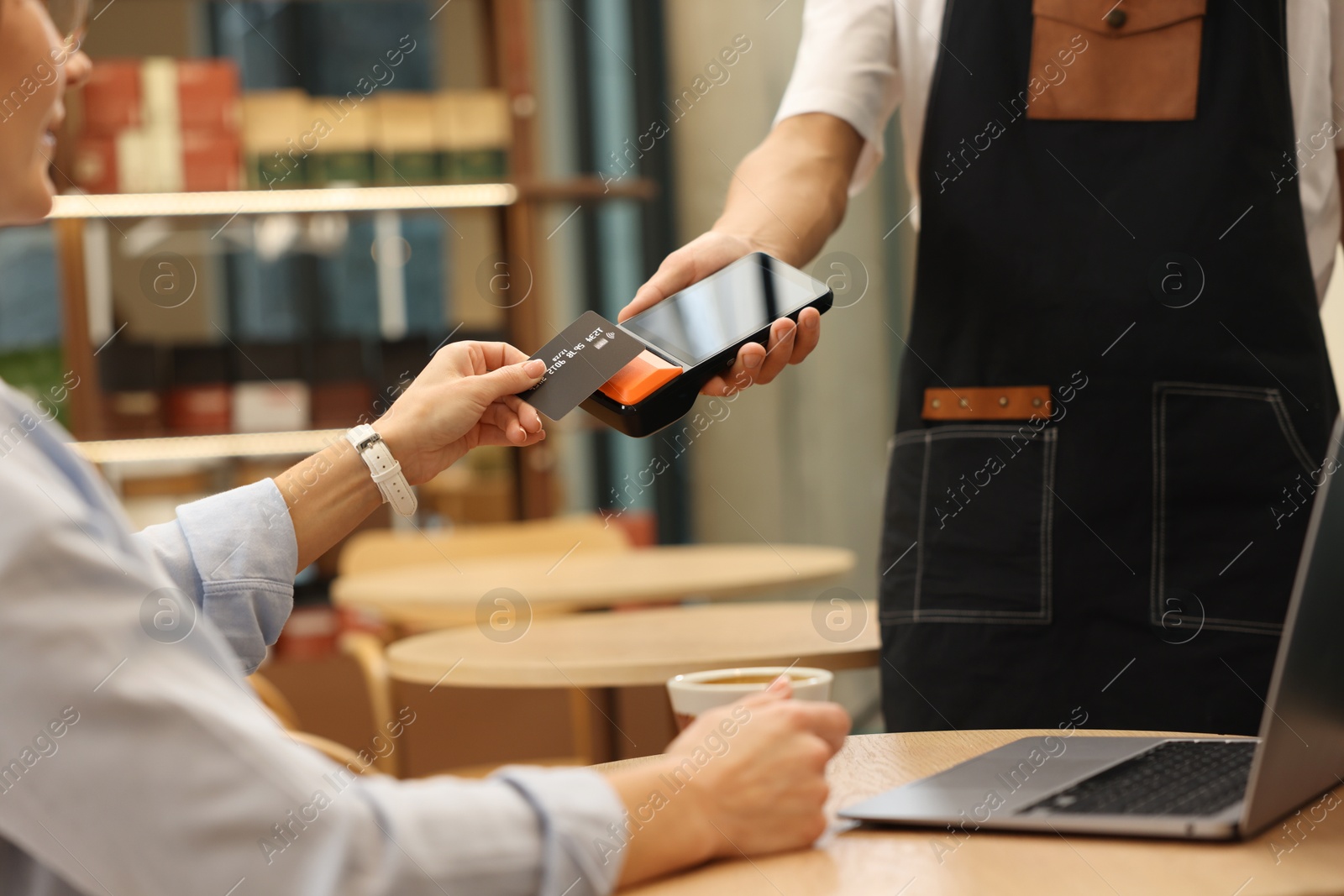 Photo of Woman paying with credit card via terminal at wooden table in cafe, closeup