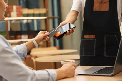 Photo of Woman paying with credit card via terminal at wooden table in cafe, closeup