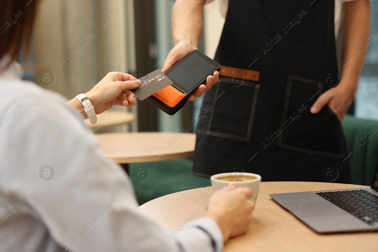 Photo of Woman paying with credit card via terminal at wooden table in cafe, closeup