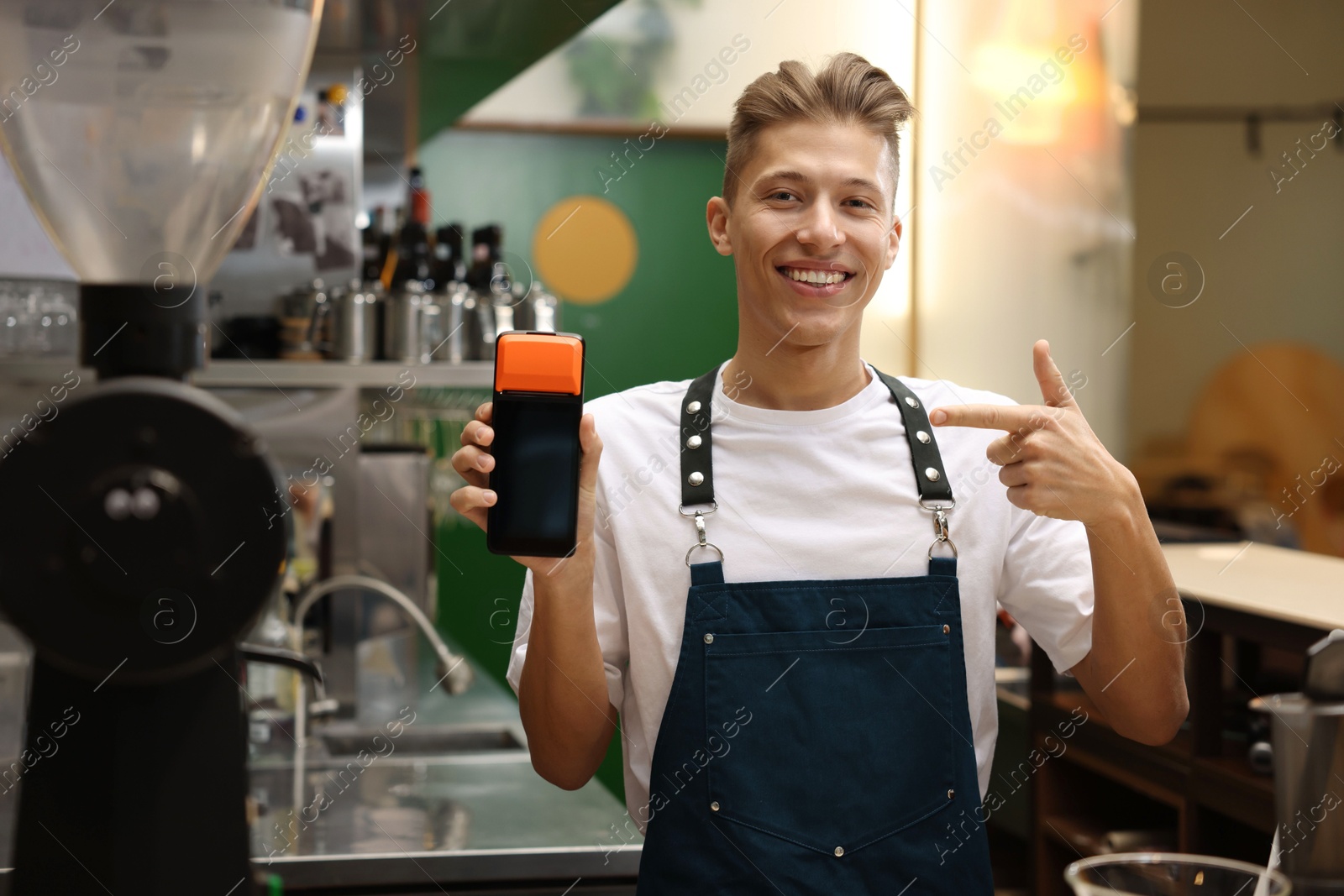 Photo of Smiling cafe worker pointing at payment terminal indoors