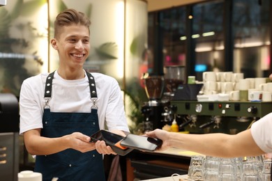 Photo of Cafe worker taking payment from client via terminal indoors