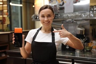 Photo of Smiling cafe worker pointing at payment terminal indoors