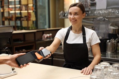 Photo of Cafe worker taking payment from client via terminal indoors