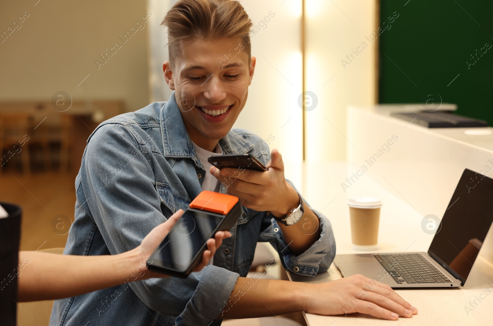 Photo of Man paying with smartphone via terminal in cafe