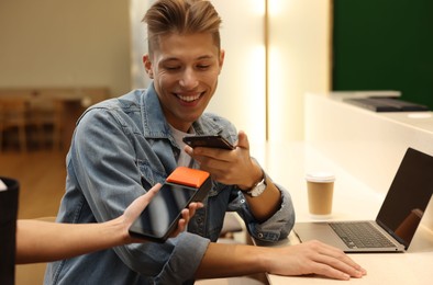 Photo of Man paying with smartphone via terminal in cafe