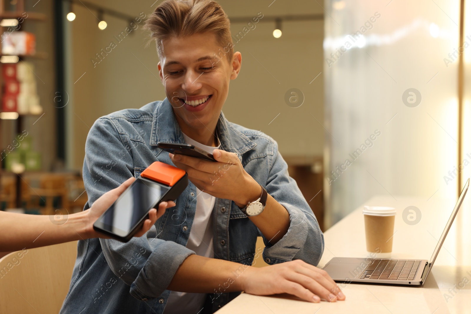 Photo of Man paying with smartphone via terminal in cafe