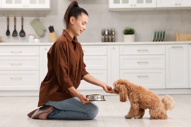 Photo of Smiling owner feeding her cute dog with dry pet food in kitchen