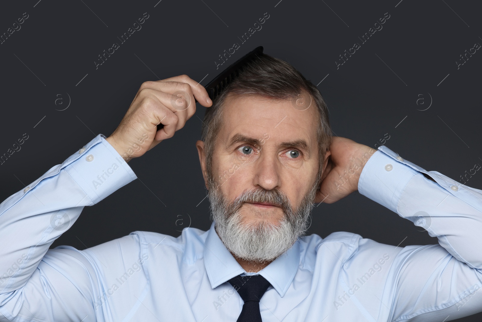 Photo of Handsome man combing his hair on dark grey background