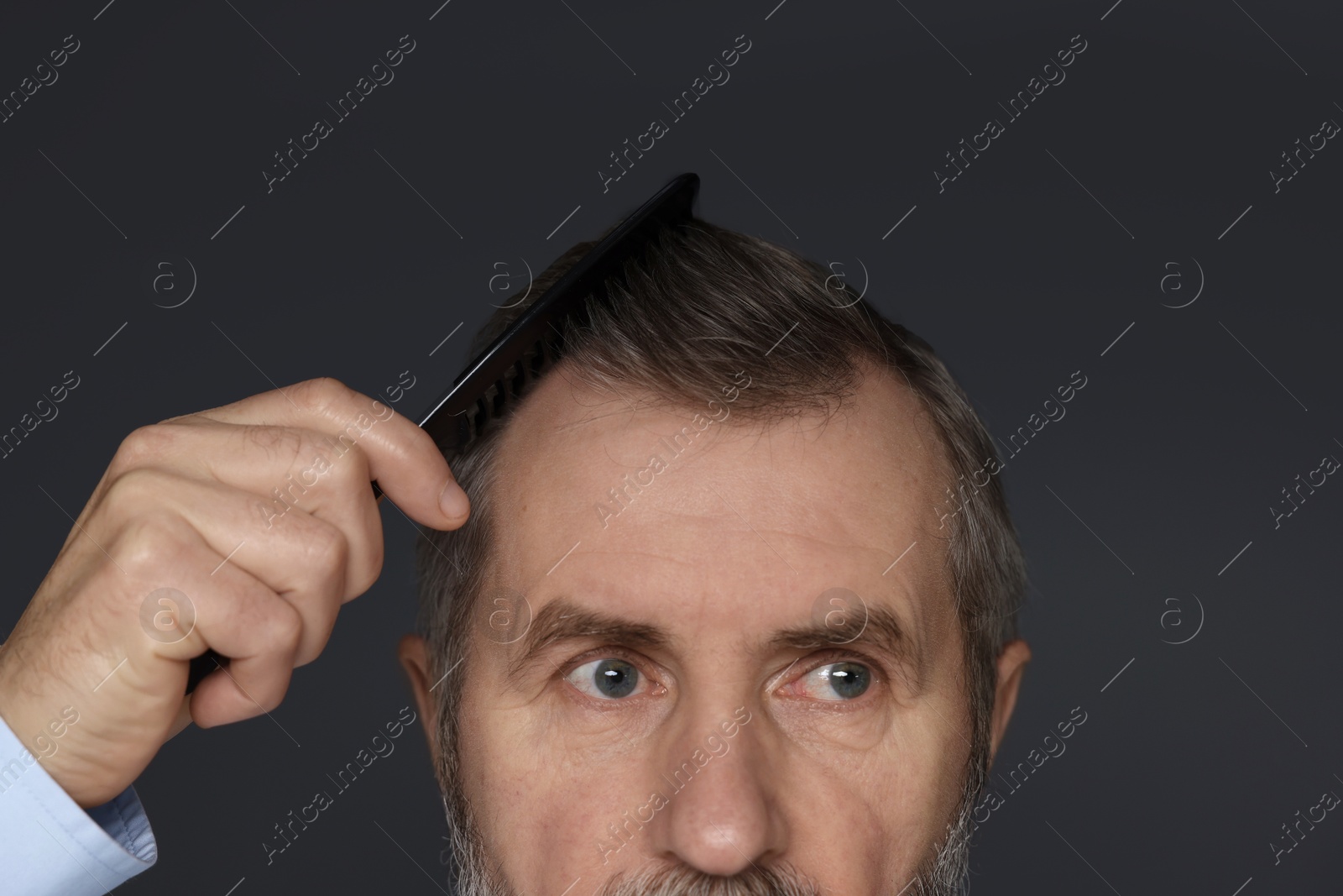 Photo of Man combing his hair on dark grey background, closeup