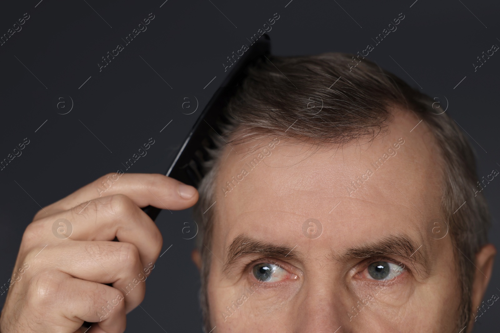 Photo of Man combing his hair on dark grey background, closeup