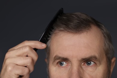 Photo of Man combing his hair on dark grey background, closeup